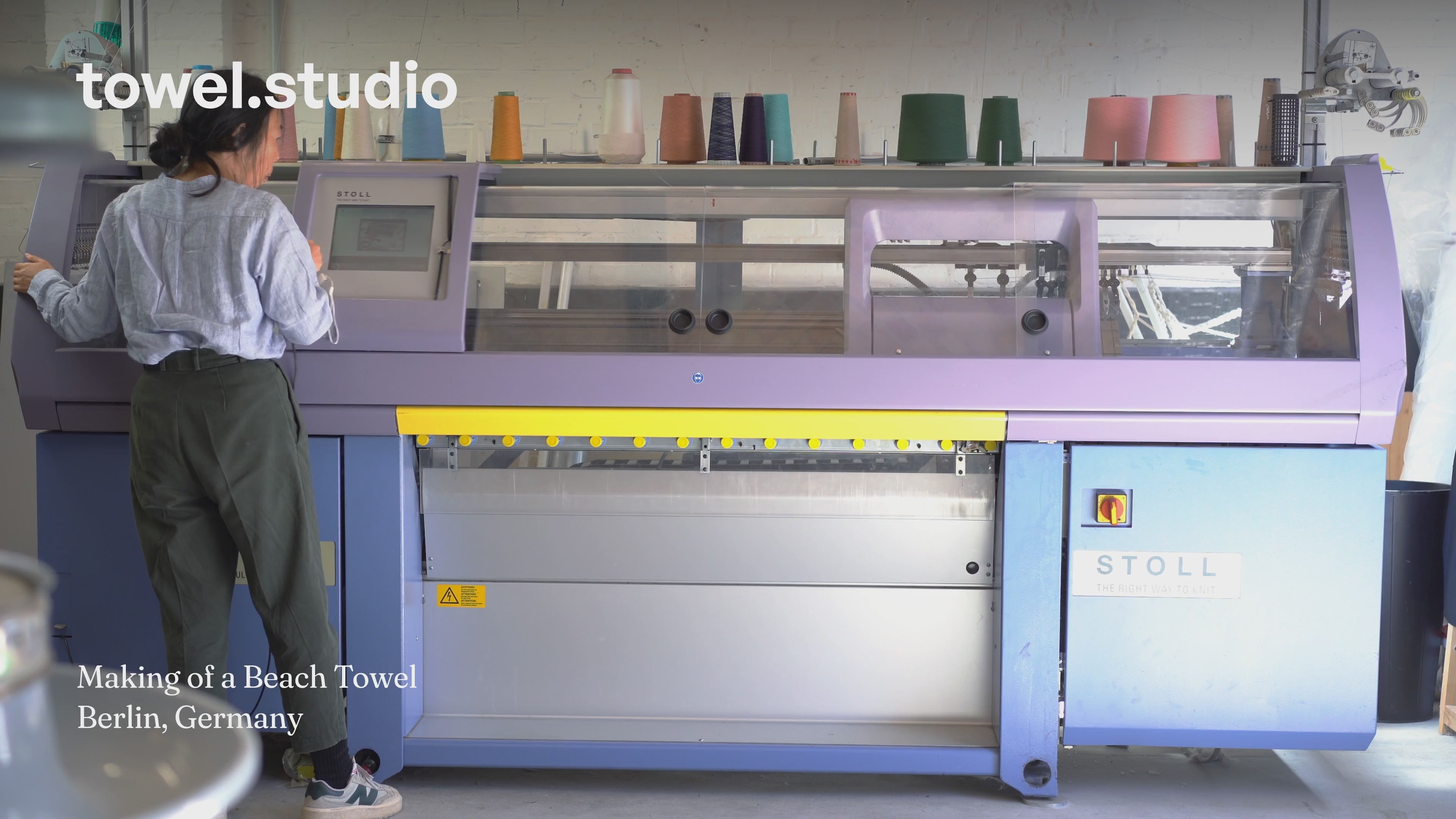 Load video: Video of a green and pink Arrow Tail Beach Towel being produced on a flat-bed knitting machine, then hand-finished in the workshop of towel.studio in Berlin, Germany.